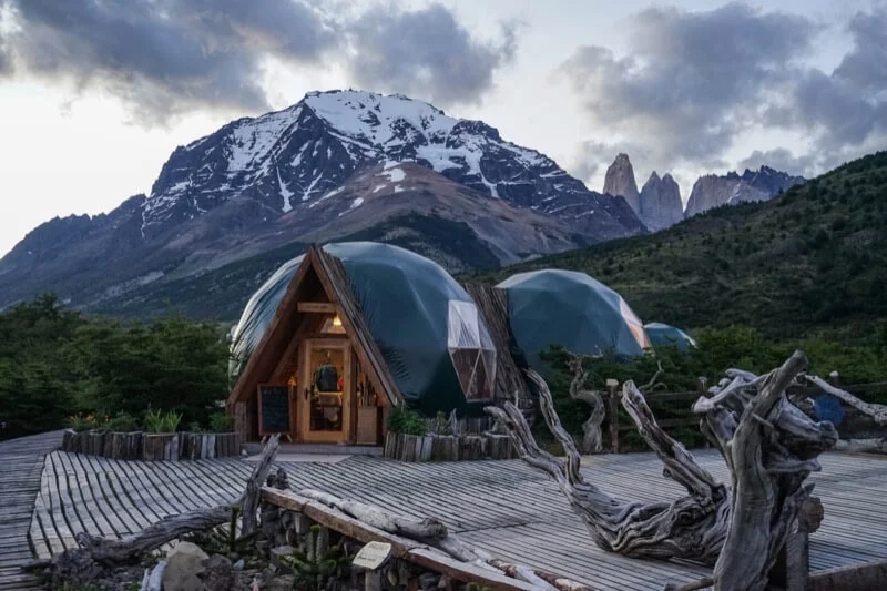 Glamping-Resort mit Kuppelzelten und Holzhütte vor schneebedeckten Bergen in der Natur