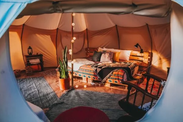Innenansicht eines gemütlich eingerichteten Glamping-Resort Zeltes mit Bett, Holzmöbeln, Pflanze und stimmungsvoller Beleuchtung