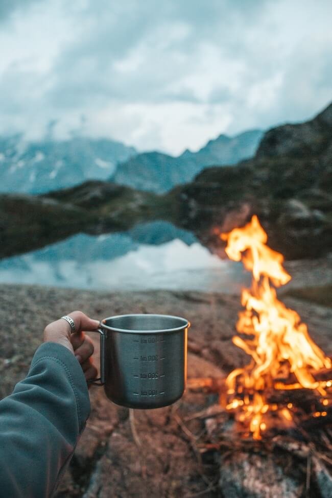 Heißes Getränk vom Campingkocher am Feuer genießen