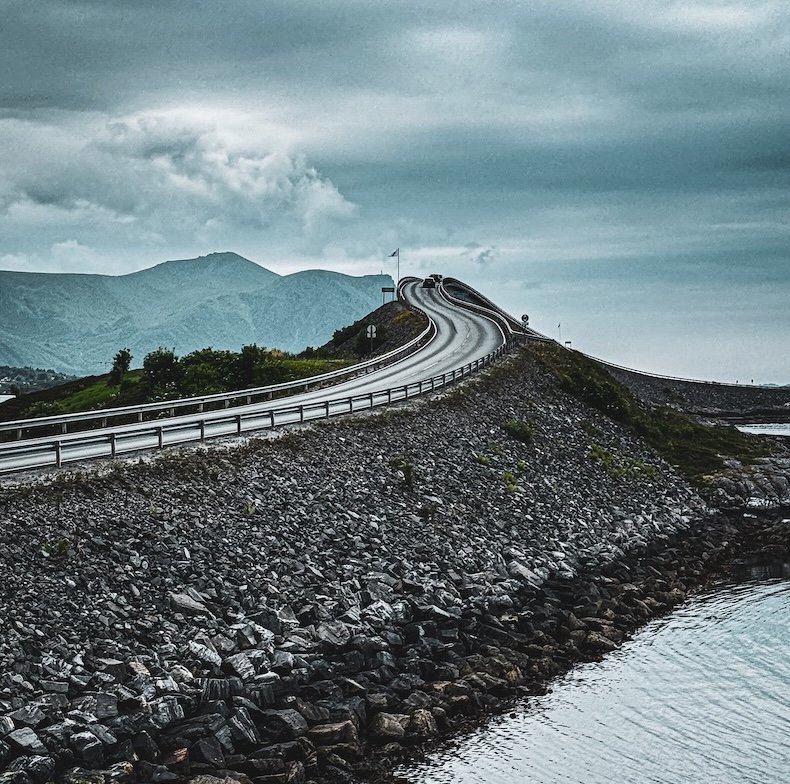 Wellenförmige Brücke der Atlantikstraße in Norwegen bei bewölktem Himmel – spektakuläre Küstenstraße mit dramatischer Kulisse.