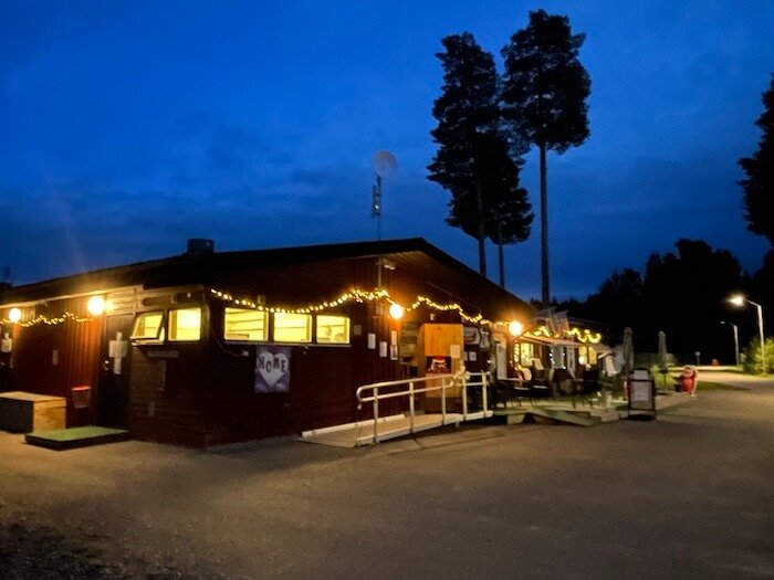 Campingplatz Lit in Jämtland, Schweden bei Nacht – Camping Lampen-bzw. Lichterkette am Holzhaus leuchtet unter dunkelblauem Himmel.
