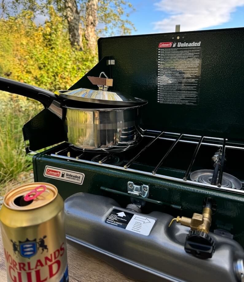 Coleman Benzinkocher im Einsatz mit Kochtopf und einer Dose Norrlands Guld im Vordergrund.