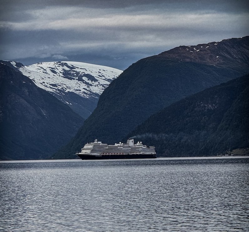 Kreuzfahrtschiff im norwegischen Fjord vor verschneiten Bergen bei dramatischer Lichtstimmung