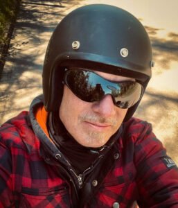 Porträt von Jojo mit mattschwarzem Helm, Sonnenbrille und rot-schwarzem Biker-Holzfällerhemd