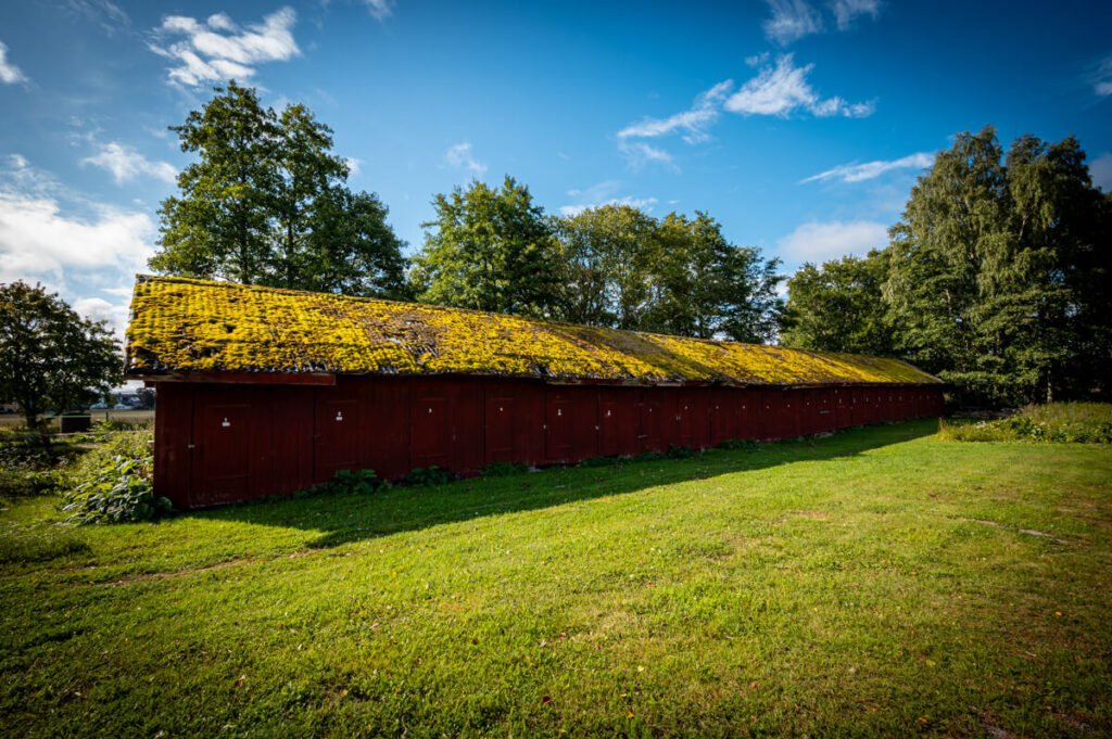 Roter Holzschuppen mit moosbedecktem Dach unter blauem Himmel in Schweden