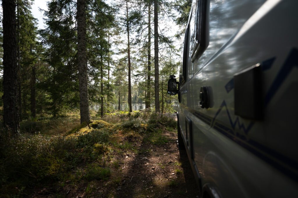„Camper am Waldrand mit Blick auf einen See in Schweden – aufgenommen aus der Seitenflucht des Fahrzeugs.“