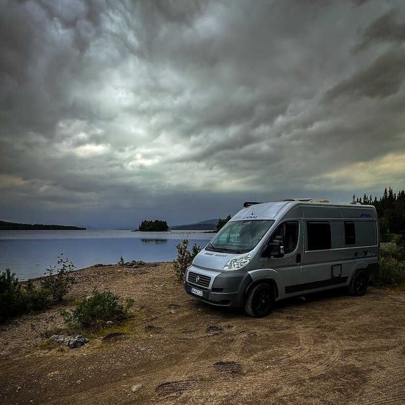 Campervan auf einem abgelegenen Stellplatz an einem See in Skandinavien, unter dramatischem Himmel.