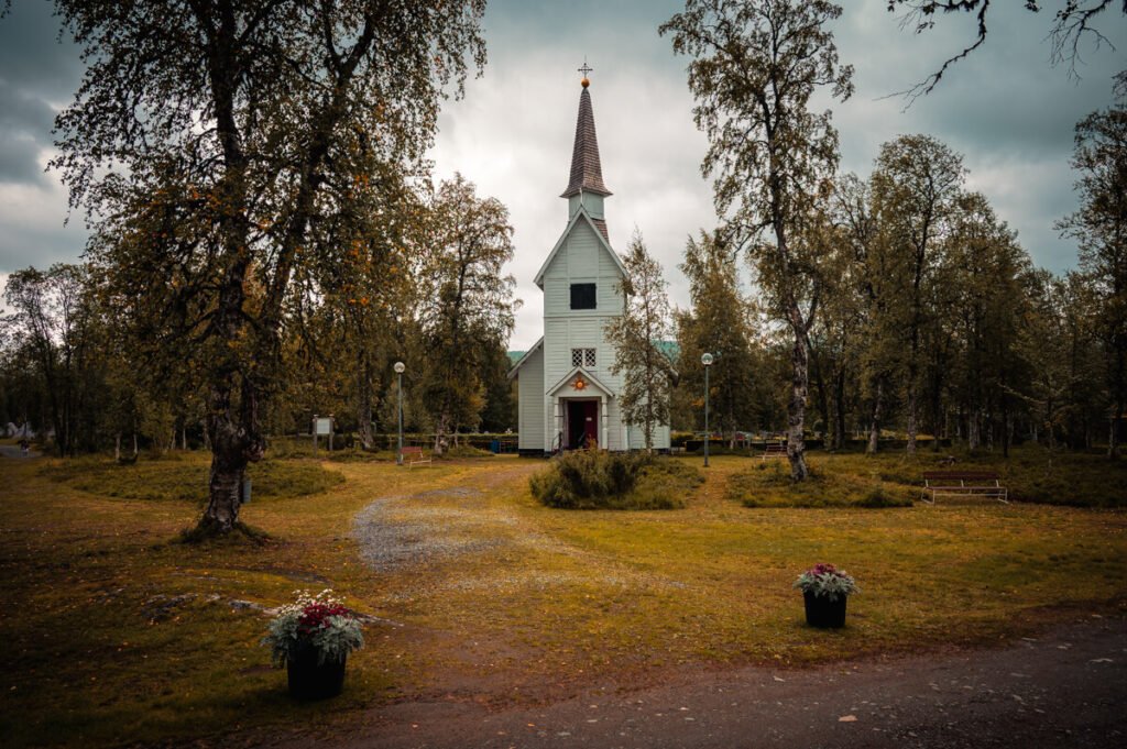 Alte Holzkirche in Lappland zwischen Bäumen, aufgenommen bei düsterem Himmel mit geheimnisvoller Atmosphäre.
