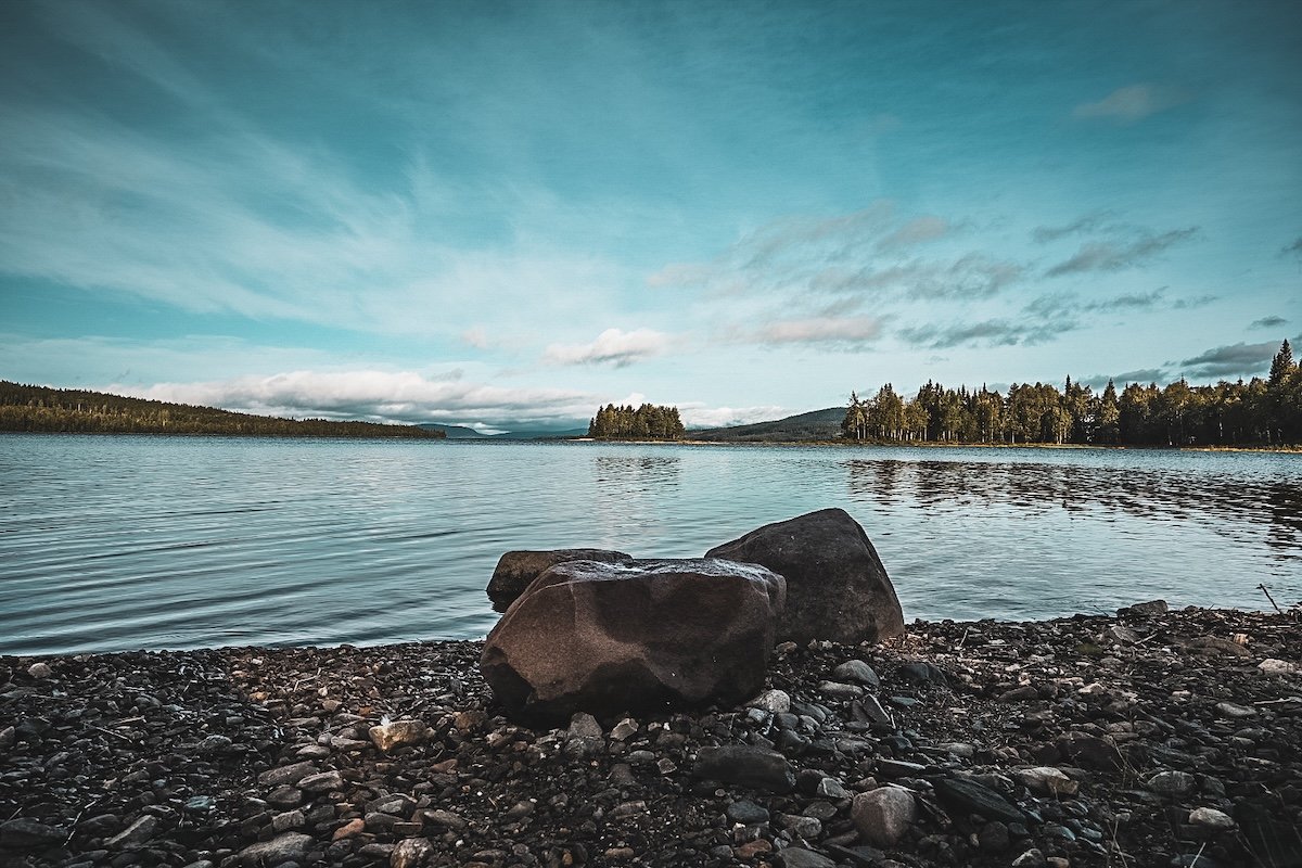 Schweden - Norwegen - Ruhiger See mit Felsen im Vordergrund und Wäldern am Horizont – typische skandinavische Landschaft