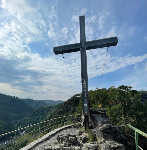 Aussichtsplattform mit dem markanten Pinnekreuz oberhalb von Cochem – mit Blick auf das grüne Moseltal unter blauem Himmel.