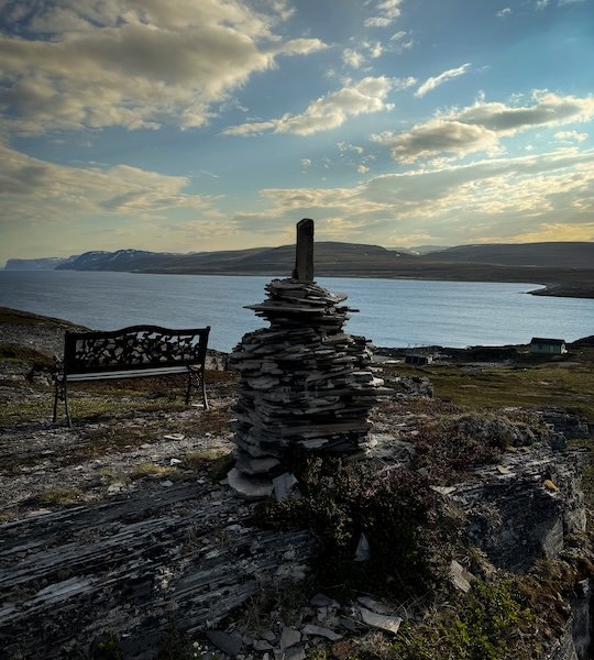 Einsame Bank und Steinhaufen mit Blick über Fjordlandschaft nahe dem Nordkap – autarkes Campen in Norwegen
