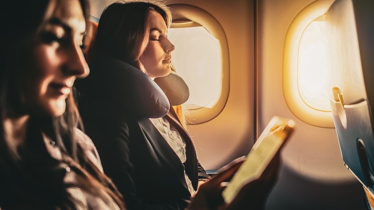 Die besten Reisekissen - Frau mit Nackenkissen im Flugzeug – entspannt schlafen auf Reisen