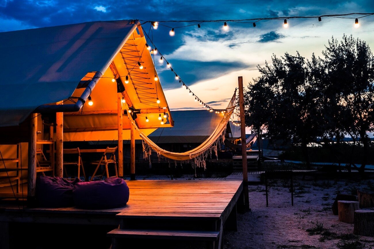 Beleuchtetes Glamping-Zelt mit Hängematte bei Sonnenuntergang – stilvolles Luxus-Camping am Meer