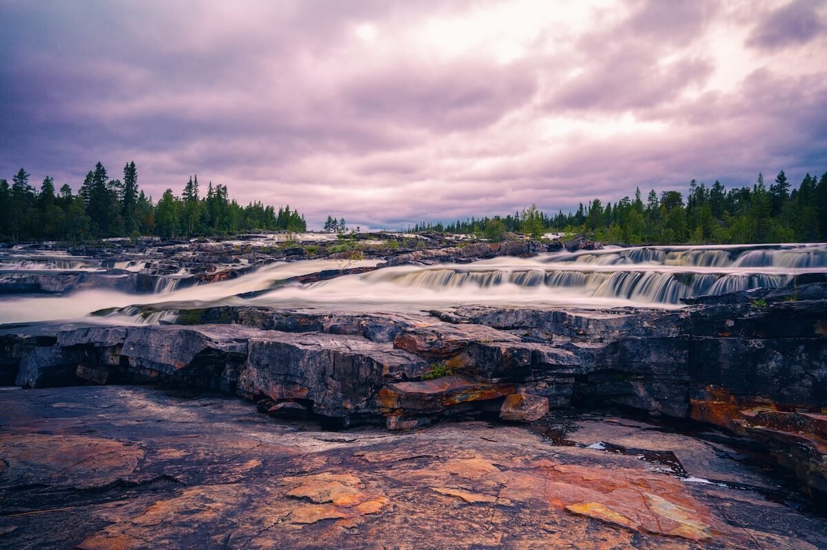 Trappstegsforsen Wasserfall in Schweden bei bewölktem Himmel mit Felsen und Wald im Hintergrund