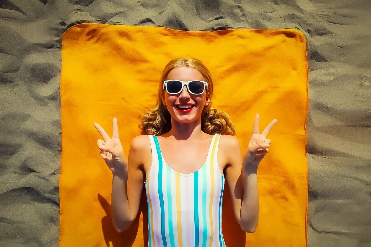 Frau liegt entspannt auf einem leuchtend orangefarbenen Mikrofaser-Camping Handtuch am Strand